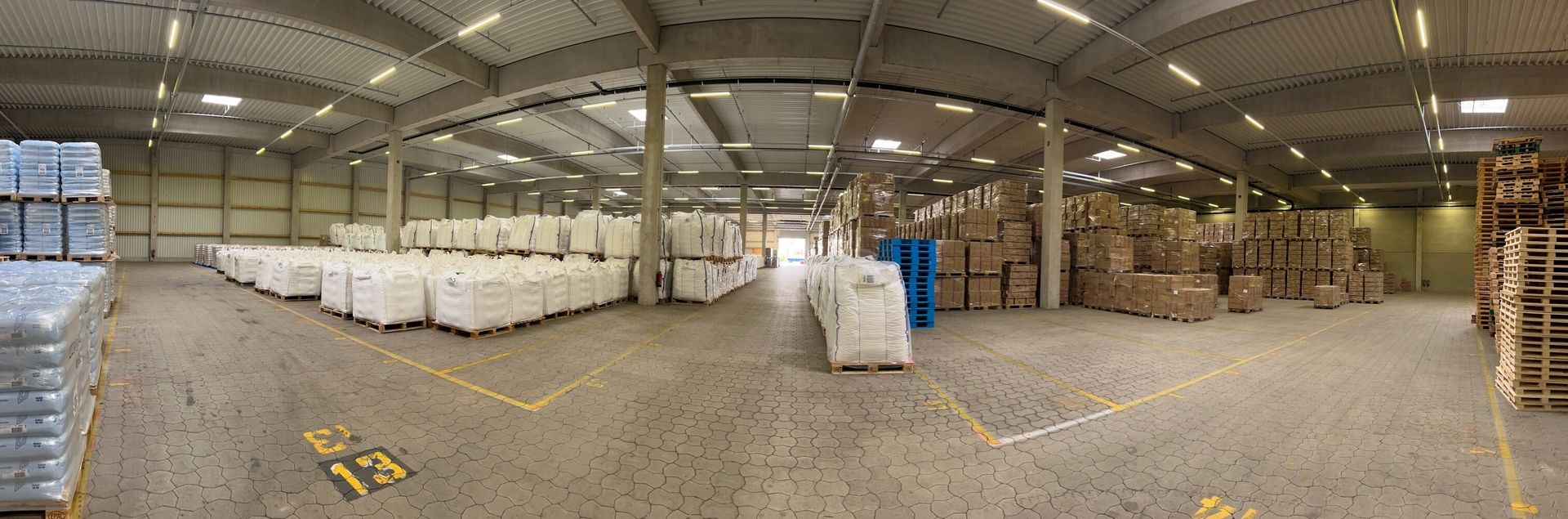 A large warehouse filled with stacked bags and boxes on pallets, showing an organized inventory and spacious layout.