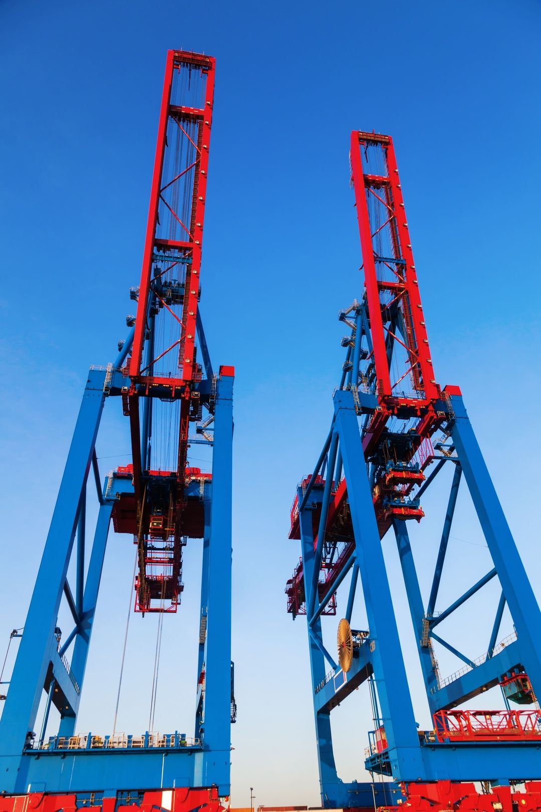 Zwei große rote und blaue Hafenkräne stehen vor einem strahlend blauen Himmel und sind für das Be- und Entladen von Fracht an einem Schiffsdock bestimmt.